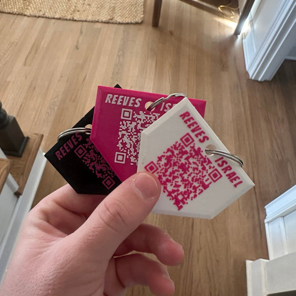 Hand holding multiple Reeves art supply tags with QR codes on a wooden floor background